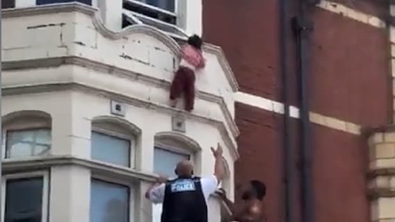 Kleinkind hängt aus Fenster über belebter Straße in Ost-London
